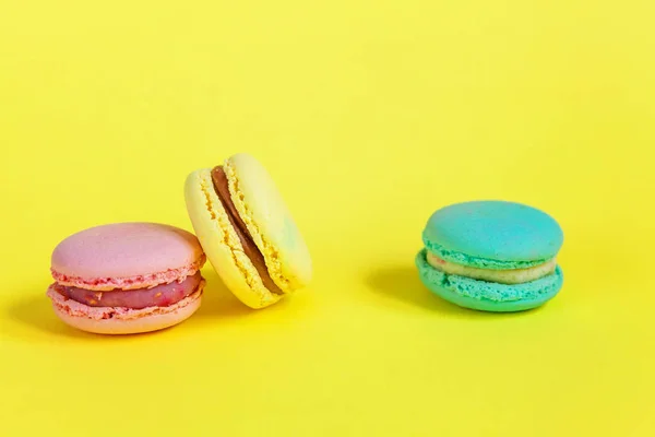 French sweet cookie. Minimal food bakery concept. Pink blue yellow green macaron on yellow background