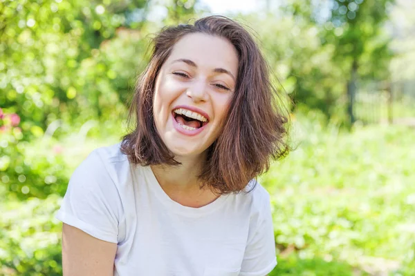 Šťastná dívka se usmívá. Krása portrét mladá šťastná, smějící se brunetka v parku nebo v zahradě — Stock fotografie
