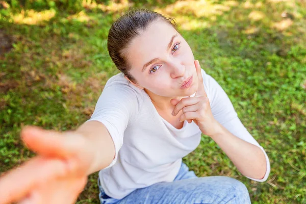Mladá srandovní dívka si bere Selži z rukou s telefonem sedícího na zeleném travním parku nebo na zahradě — Stock fotografie