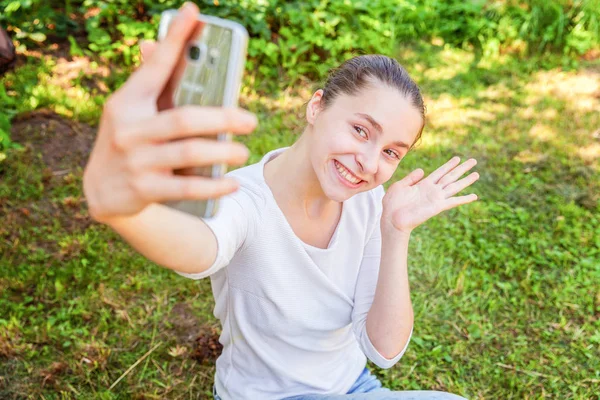 Young funny girl take selfie from hands with phone sitting on green grass park or garden background Stock Image