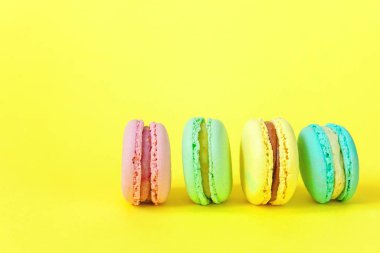 Fransız tatlı kurabiye. Çok az yiyecek ekmek kavramı. Pembe mavi sarı yeşil macaron Sarı zemin üzerine