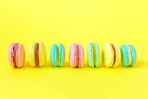 French sweet cookie. Minimal food bakery concept. Pink blue yellow green macaron on yellow background