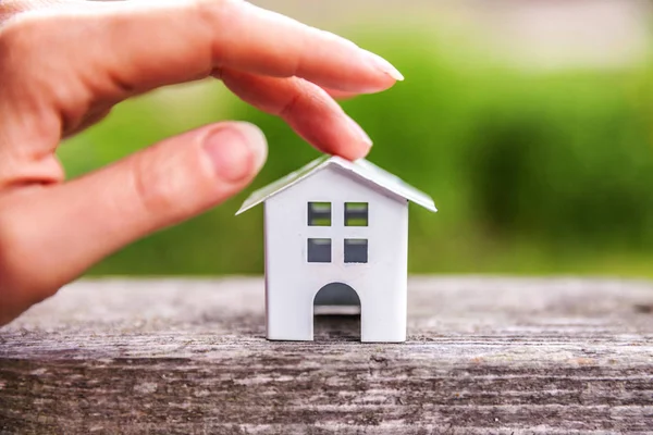 Yeşil zemin yakın ahşap arka planda minyatür beyaz oyuncak model ev ve kadın kadın el