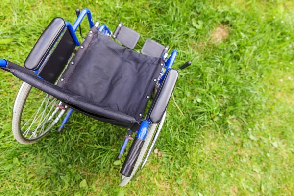 Cadeira de rodas vazia em pé na grama no parque hospitalar esperando pelos serviços do paciente — Fotografia de Stock