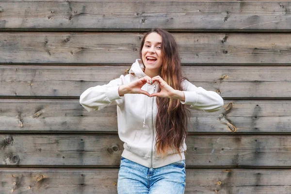 Love, heart shape, peace. Beauty portrait young happy positive woman showing heart sign with hands on wooden wall background