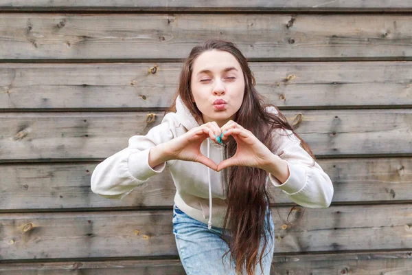 사랑, 하트 모양, 평화. 아름다움 초상화 젊은 행복 한 긍정적인 여자 보여주는 심장 기호 와 손 에 나무 벽 배경 — 스톡 사진