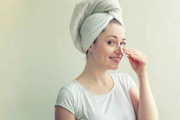 Lachende vrouw in handdoek op hoofd met zachte gezonde huid verwijderen make-up met wattenschijfje geïsoleerd op witte achtergrond — Stockfoto