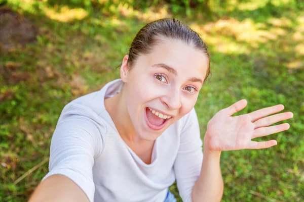 Jovem garota engraçada tirar selfie de mãos com telefone sentado no parque de grama verde ou jardim de fundo — Fotografia de Stock