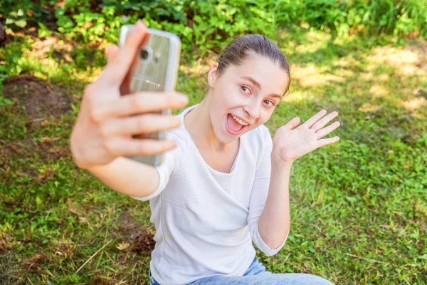 Young funny girl take selfie from hands with phone sitting on green grass park or garden background Royalty Free Stock Photos
