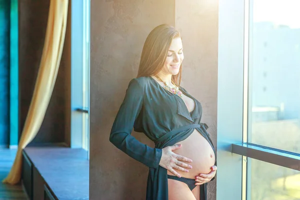 Pregnancy woman standing near window at home and smiles