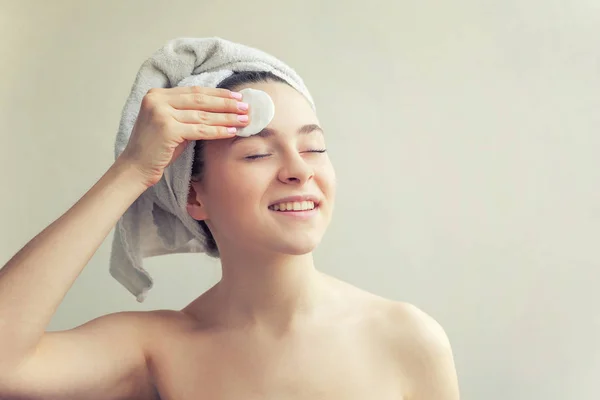 Usměvavá žena v ručníku na hlavě s jemnou zdravou kůží s bavlněnou destkou, izolovanou na bílém pozadí — Stock fotografie