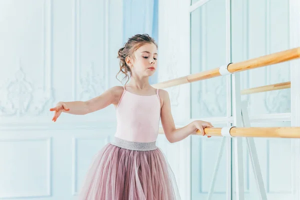 Hermosa bailarina elegante practica posiciones de ballet en falda tutú rosa en clase de baile —  Fotos de Stock