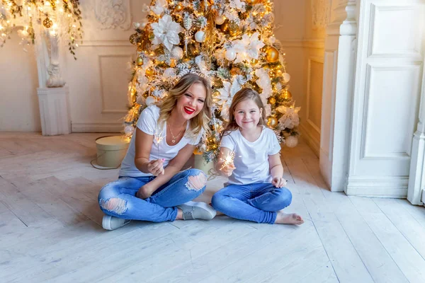Счастливая семья женщина мать и маленькая девочка расслабиться играть искры возле елки в канун Рождества дома — стоковое фото