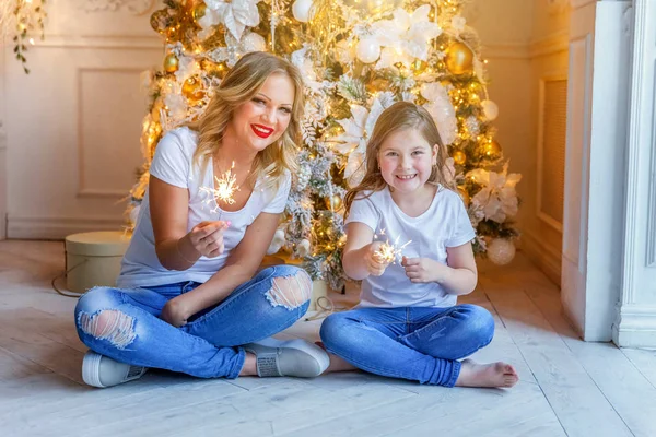 Счастливая семья женщина мать и маленькая девочка расслабиться играть искры возле елки в канун Рождества дома — стоковое фото