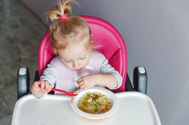 Kirli yüzü ile bebek kız evde mutfakta yüksek bebek sandalyede kaşıkla çorba kendisi yeme