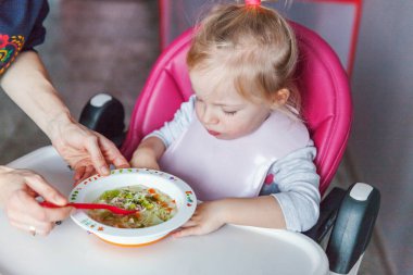 Evde mutfakta yüksek bebek sandalyede kaşıkla bebek kız besleme anne