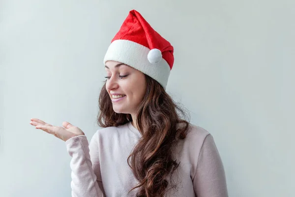Belle fille en chapeau rouge du Père Noël montrant la main ouverte de la paume réconfortée sur fond blanc — Photo