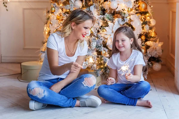 Feliz família mulher mãe e menina relaxar jogando sparkler perto da árvore de Natal na véspera de Natal em casa — Fotografia de Stock