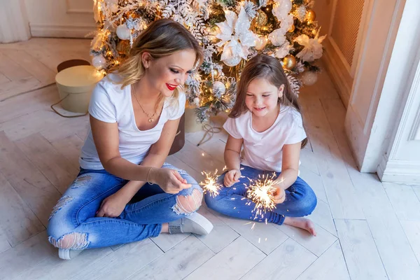 Feliz família mulher mãe e menina relaxar jogando sparkler perto da árvore de Natal na véspera de Natal em casa — Fotografia de Stock