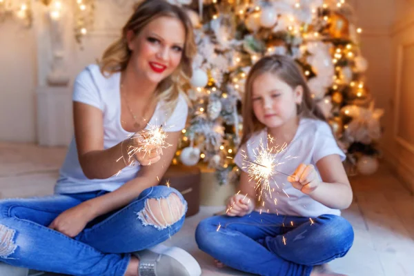 Feliz família mulher mãe e menina relaxar jogando sparkler perto da árvore de Natal na véspera de Natal em casa — Fotografia de Stock