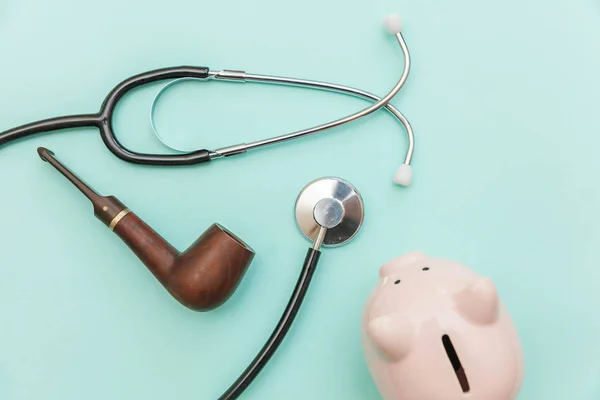 Conceito de saúde do homem. Equipamento de medicina estetoscópio ou fonendoscópio fumar cachimbo porquinho banco isolado no moderno fundo azul pastel — Fotografia de Stock