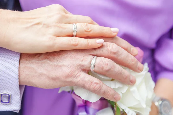 Braut und Bräutigam Hände mit Eheringen vor dem Hintergrund des Brautstraußes aus Blumen — Stockfoto