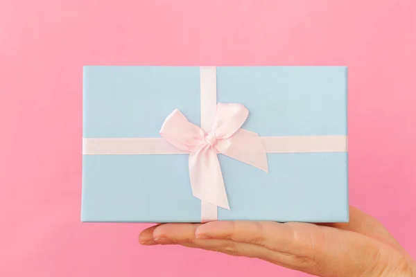 Simplemente diseñe la mano femenina de la mujer que sostiene la caja de regalo azul aislada en un fondo de moda colorido pastel rosa —  Fotos de Stock