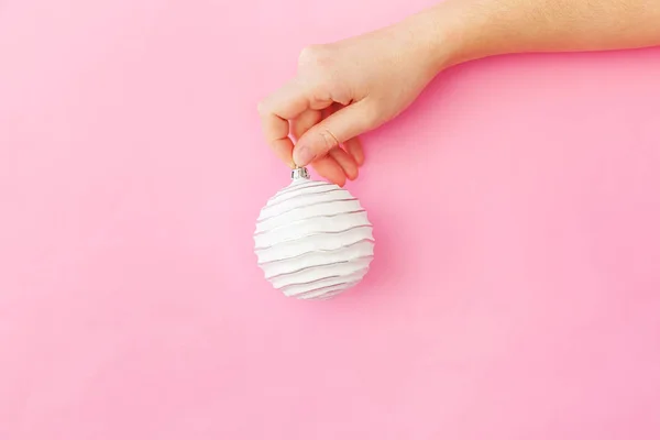 Просто минимальный дизайн женская рука держа Рождественский орнамент мяч изолирован на розовый пастель красочный модный фон — стоковое фото