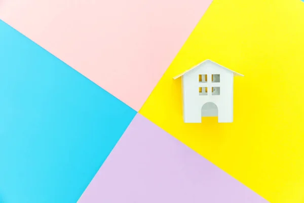 Miniature white toy house isolated on blue yellow pink purple pastel colorful trendy geometric background