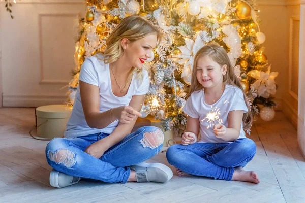 Feliz família mulher mãe e menina relaxar jogando sparkler perto da árvore de Natal na véspera de Natal em casa — Fotografia de Stock