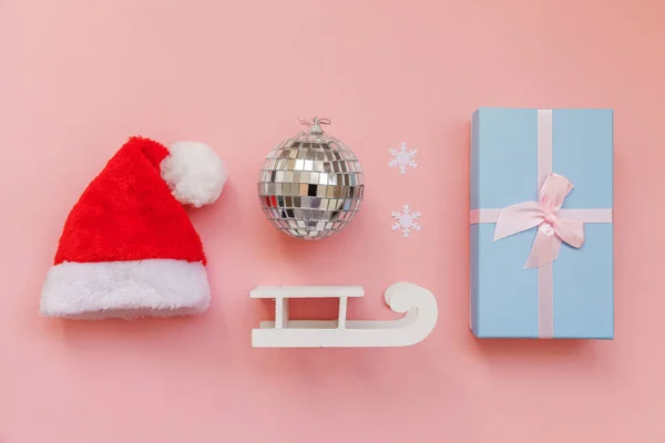 Simplesmente composição mínima objetos de inverno ornamento chapéu de Santa trenó caixa de presente isolado no fundo da moda pastel rosa — Fotografia de Stock