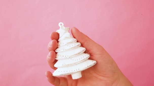 ピンクのパステルカラフルなトレンディな背景に隔離されたクリスマスオーナメントモミの木を保持するシンプルなデザインの女性の手 — ストック動画