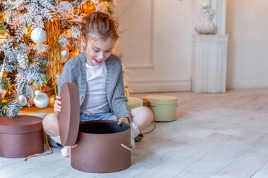 Evde Noel ağacının yanında hediye kutusu olan küçük kız.