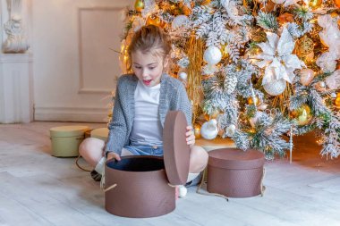Evde Noel ağacının yanında hediye kutusu olan küçük kız.