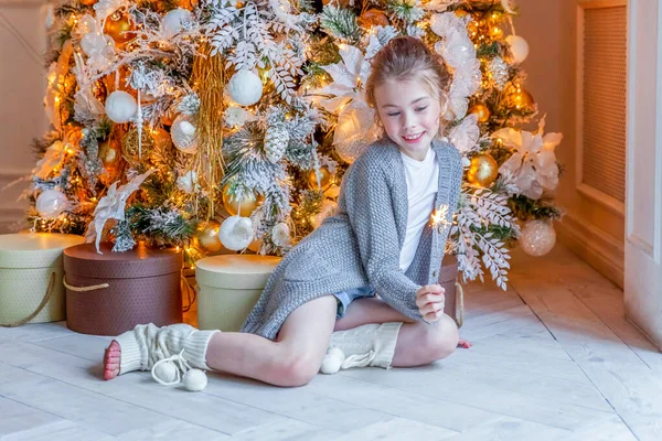 Little girl with sparkler near Christmas tree at home — ストック写真