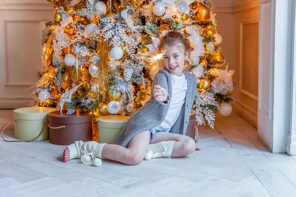 Little girl with sparkler near Christmas tree at home — ストック写真