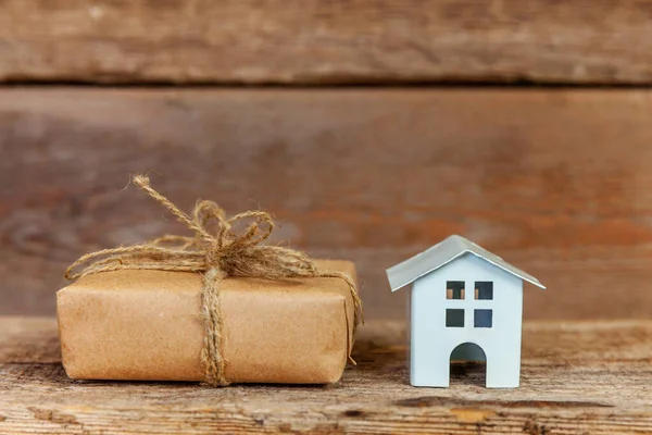 Миниатюрный белый игрушечный домик и подарочная коробка на деревянном фоне — стоковое фото