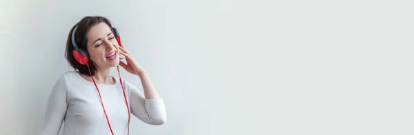 Energía joven morena dama mujer escuchando música en los auriculares y cantando aislado en el banner de fondo blanco —  Fotos de Stock