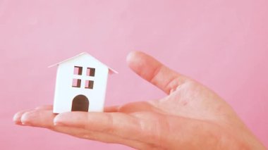 Sadece pembe pastel renkli trendy arka plan izole minyatür beyaz oyuncak ev tutan kadın kadın el tasarımı. Mortgage emlak sigortası rüya ev kavramı. Kopyalama alanı