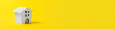 Minyatür beyaz oyuncak evi olan basit bir tasarım sarı renkli arka planda izole edilmiş. Ev kredisi sigortası hayali ev konsepti. Düz görünüm fotokopi alanı pankartı.