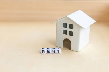 Minyatür oyuncak model evi. Üzerinde tahta zemin üzerine yazılmış RENT harfleri var. Eco Village soyut çevre geçmişi. Gayrimenkul ipoteği sigortası tatlı ev ekoloji kira kavramı