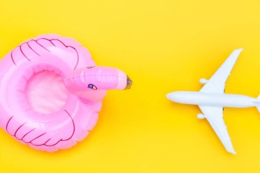 Yaz kumsalı kompozisyonu. Uçak ve sarı zemin üzerinde izole edilmiş şişirilebilir flamingo ile minimum basit düz yatıyordu. Seyahat macerası konsepti. Üst görünüm kopyalama alanı