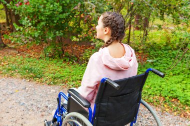 Hastane parkında tekerlekli sandalyedeki genç mutlu engelli kadın hasta hizmetlerini bekliyor. Doğadaki engelli insanlar için sakat sandalyeli felçli bir kız. Rehabilitasyon kavramı