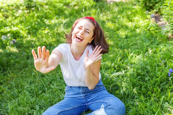 야외에서 미소짓는 행복 한 소녀. 갈색 털을 가진 아름다운 젊은 브루 네 테 여인은 공원이나 푸른 잔디 위에 앉아 있다. 유럽 여성. 긍정적 인 인간의 표정 표정 표정 표정. — 스톡 사진