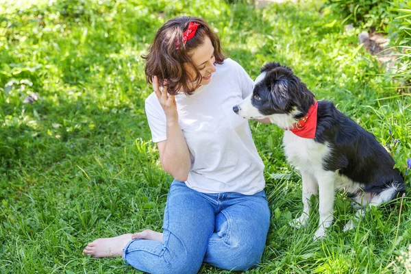 Smiling young attractive woman playing with cute puppy dog border collie in summer garden or city park outdoor background. Girl training trick with dog friend. Pet care and animals concept. — Stock Photo, Image