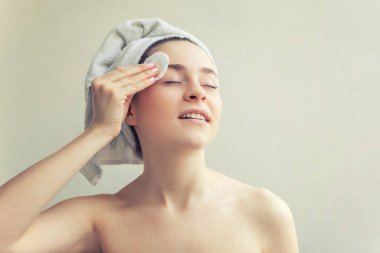 Kafasında havlu olan, yumuşak, sağlıklı derili, beyaz arka planda izole edilmiş pamuk yastıkla makyaj yapan güzel bir kadın portresi. Cilt temizleme spa rahatlama konsepti