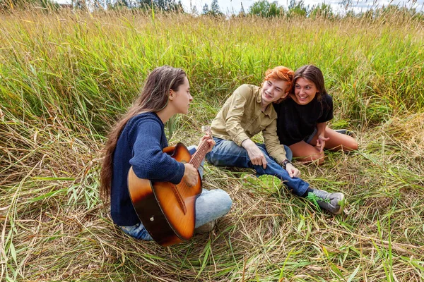Summer holidays vacation music happy people concept. Group of three friends boy and two girls with guitar singing song having fun together outdoors. Picnic with friends on road trip in nature