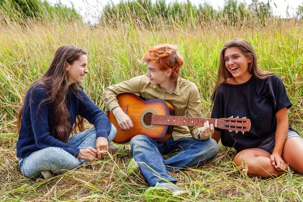 Summer holidays vacation music happy people concept. Group of three friends boy and two girls with guitar singing song having fun together outdoors. Picnic with friends on road trip in nature