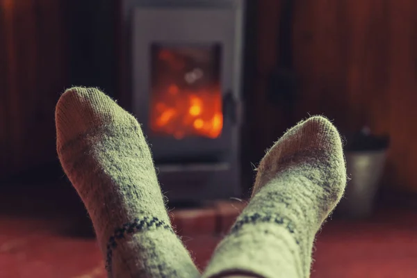 Feet legs in winter clothes wool socks at fireplace background. Woman sitting at home on winter or autumn evening relaxing and warming up. Winter and cold weather concept. Hygge Christmas eve