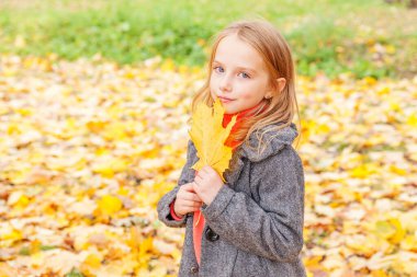 Sarı yapraklarla oynayan mutlu genç bir kız güzel bir sonbahar parkında doğa yürüyüşünde. Sonbahar portakal yaprağı tutan küçük çocuk.